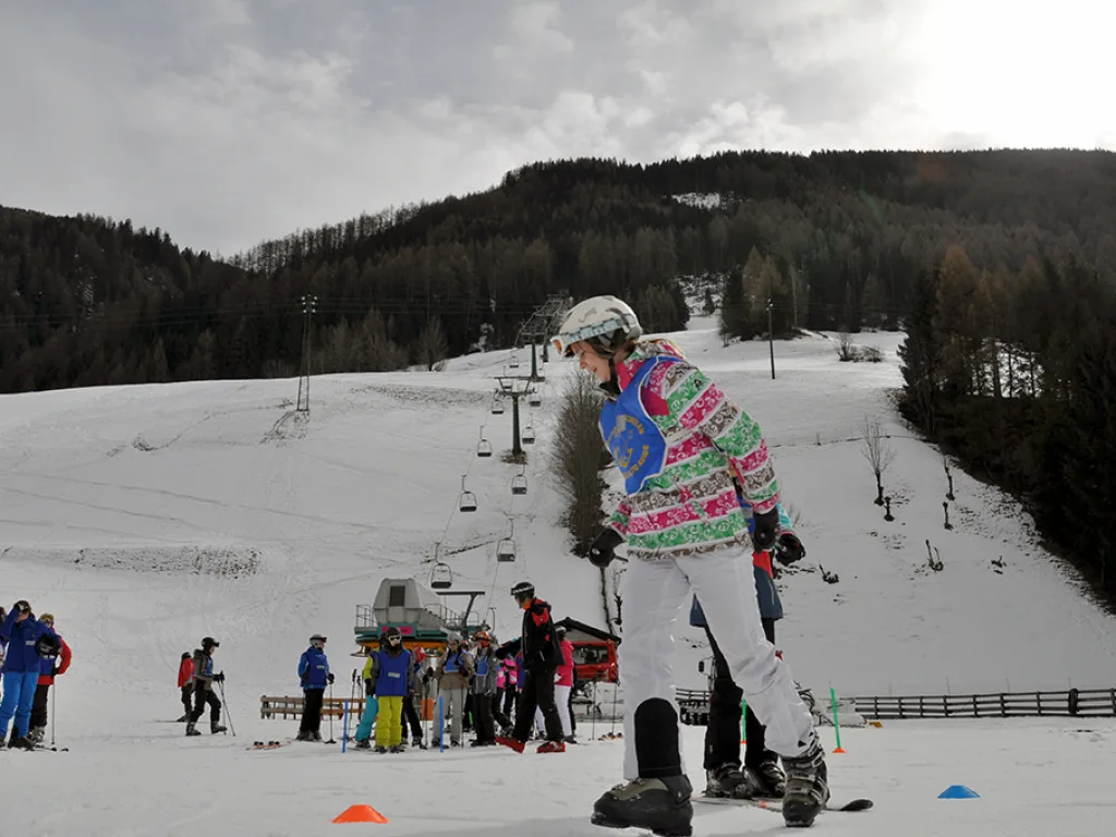 Snowboarderin steht am Pistenrand vor dem Sessellift.